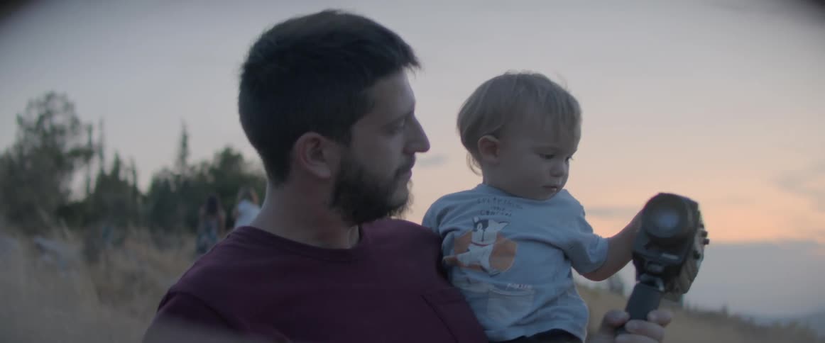 A man outside holding a baby and a camera with two women in the background