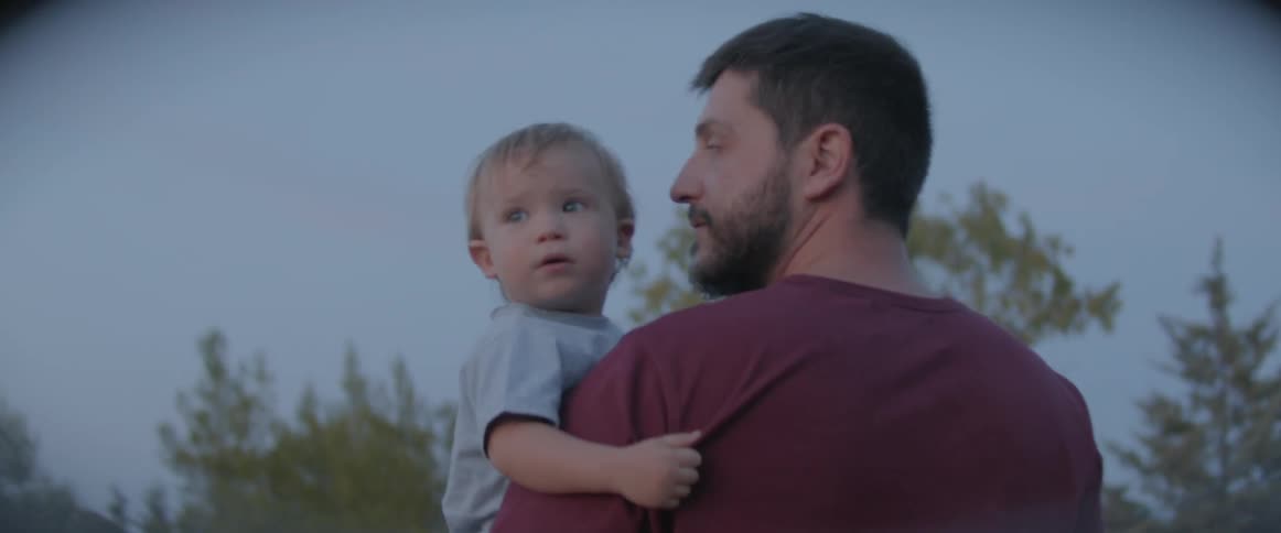 Father holding son outdoors near trees at sunset