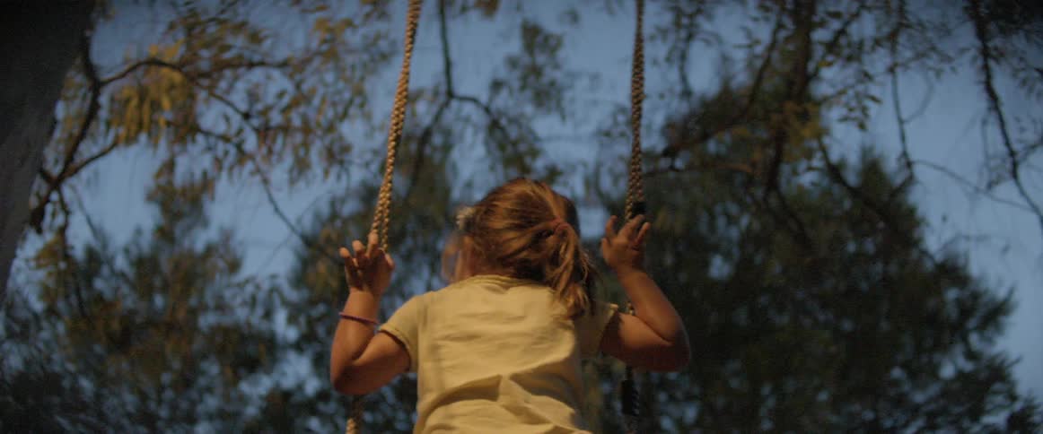 Little girl swinging from a swing under a large tree