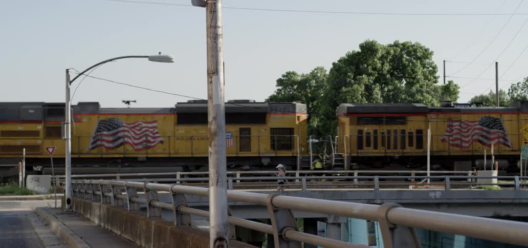 A large freight train slowly makes it was through a town as a female pedestrian walks by on the street