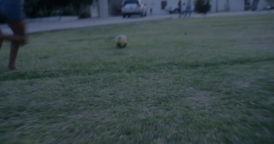 Two girls running in the grass kicking a soccer ball