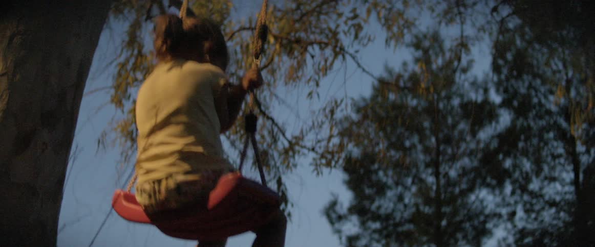 Little girl swings under tree at dusk