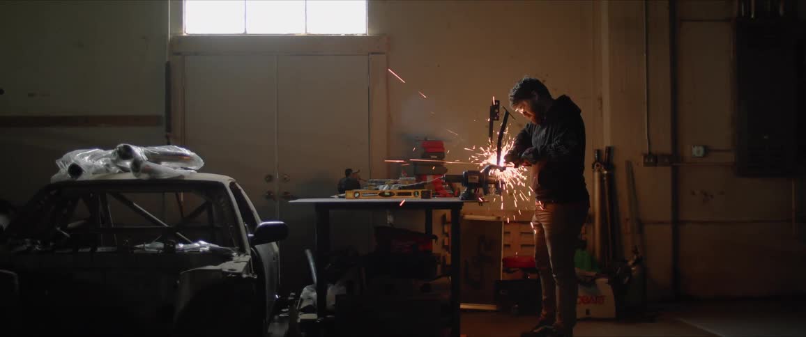 A man uses an angle grinder in a work shop creating a shower of sparks