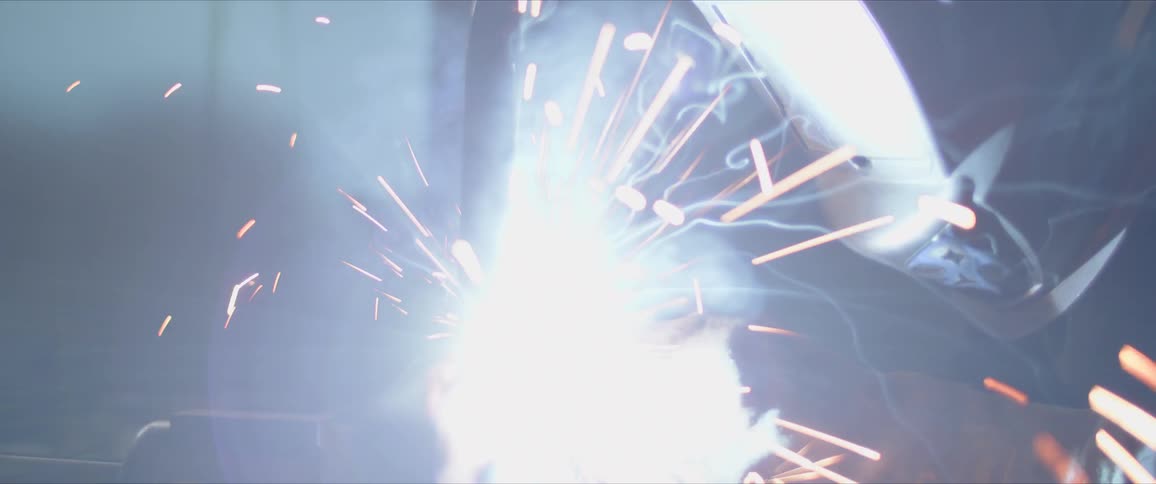 A welder with a helmet works with metal in a garage