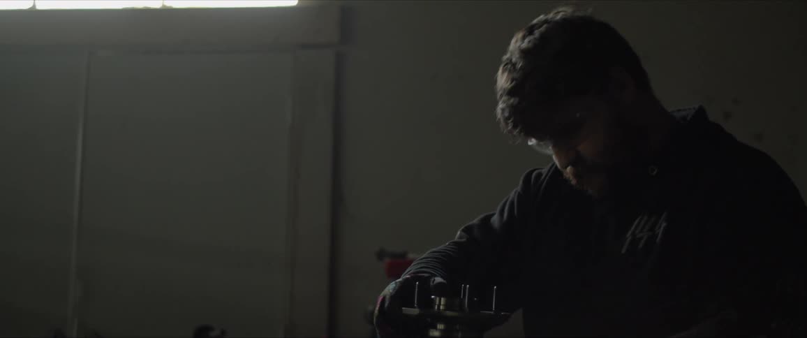 A man in a garage lifts an object and hammers bolts into it