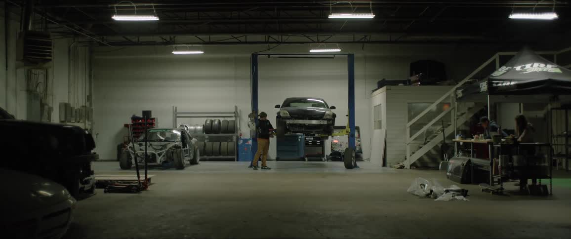 A man takes a tire off of a car on an elevated lift