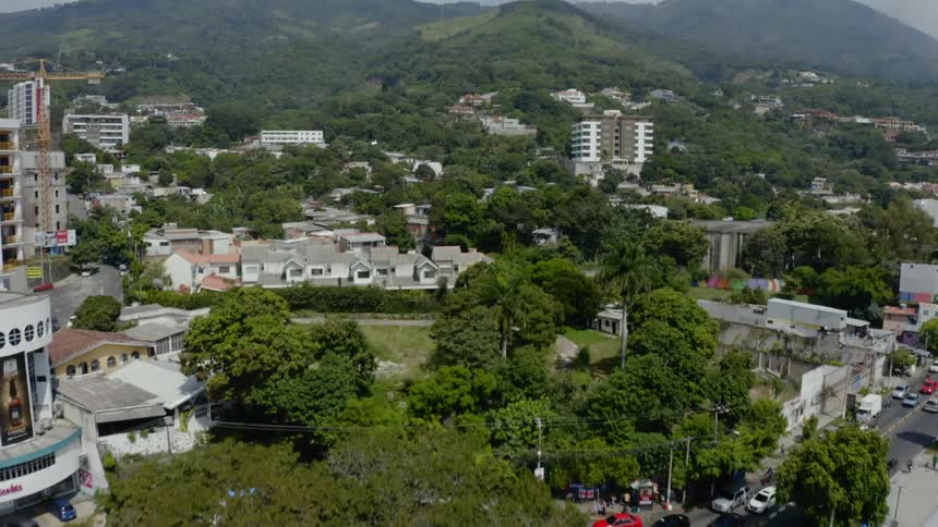 Cars travel around a traffic circle in a town square with hills on the horizon