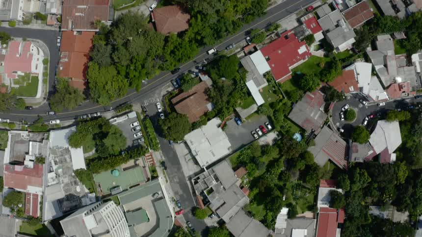 Cars travel on roads past homes and buildings in a neighborhood on a sunny day