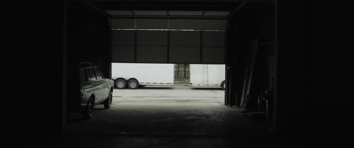 A man in a garage walks and closes the door