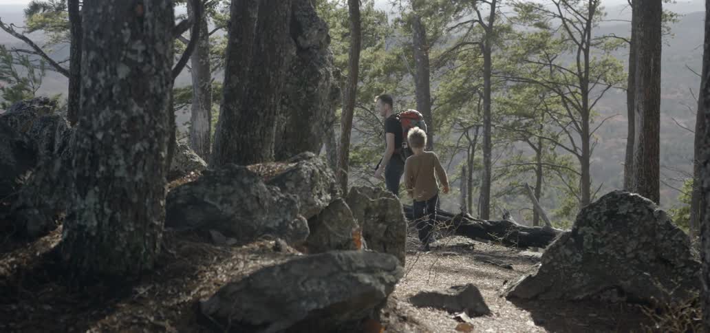 A child walks behind a father as they hike in the woods