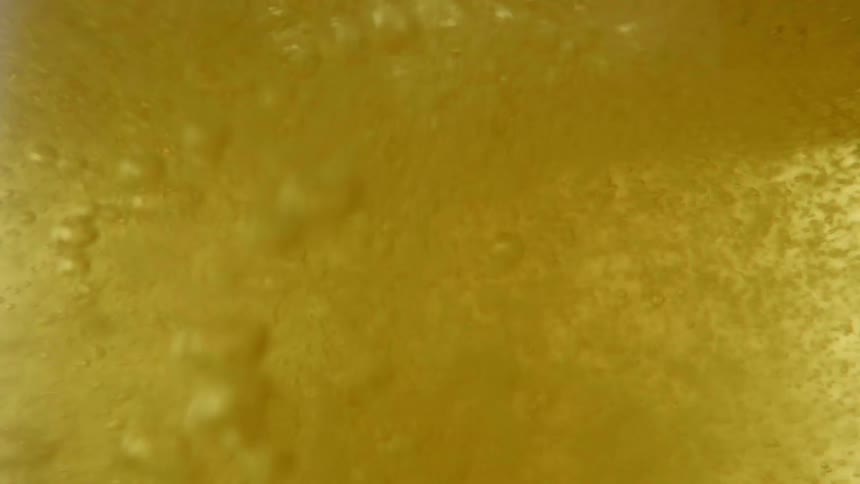 Air shoots into the surface of golden liquid creating a tumultuous torrent of liquid