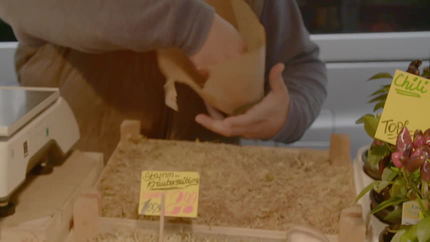 A person in a store taking mushrooms and putting it in a brown paper bag