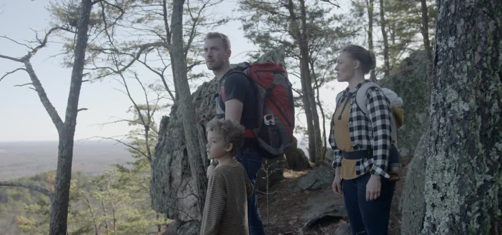 A family of three stand high on a hill as they hike in the woods