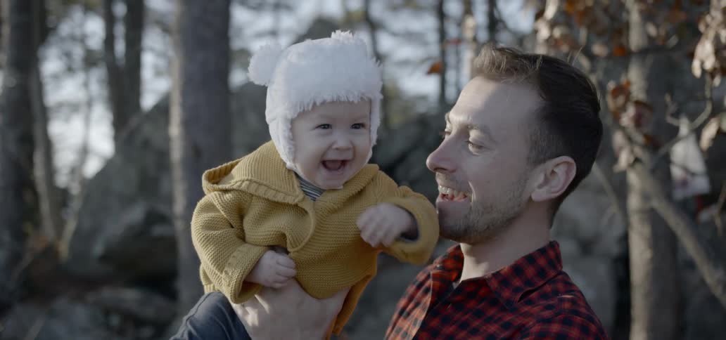 A man holding a baby up out in a forest