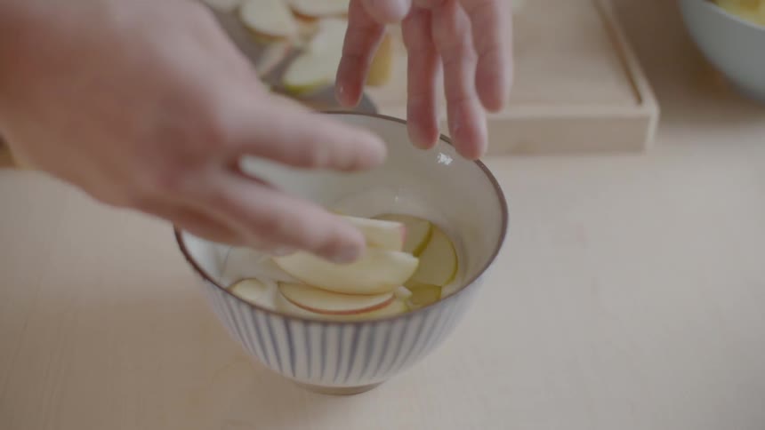 A person drops apple slices in to a bowl