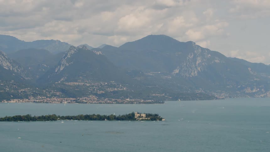 A house sits on a small island in the ocean near a mountain range