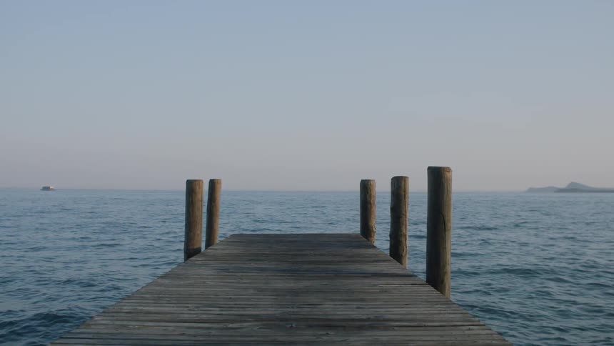 A wooden dock with posts in the ocean and a boat off in the distance