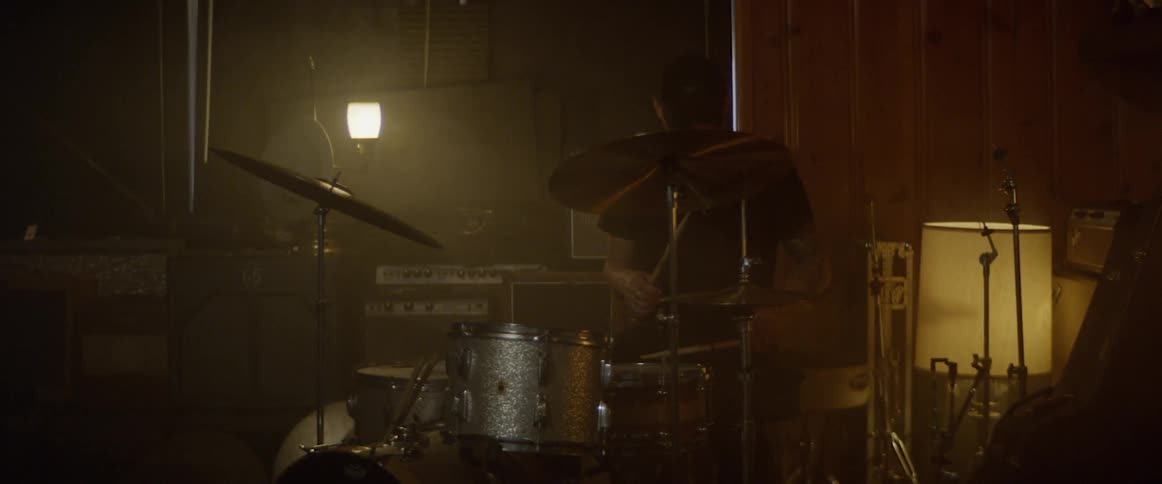Man playing drums indoors in the dark with a small light on