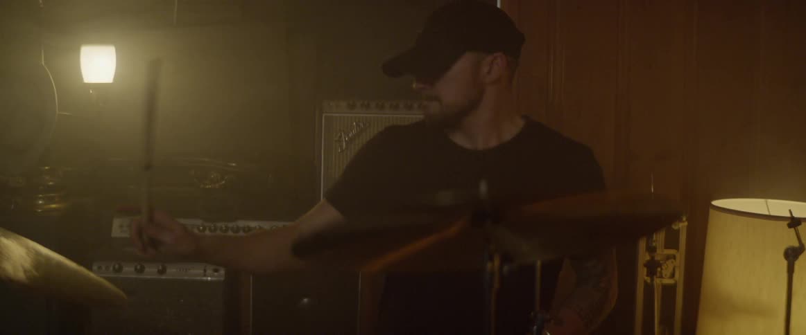 A man with a black hat and t shirt playing the drums