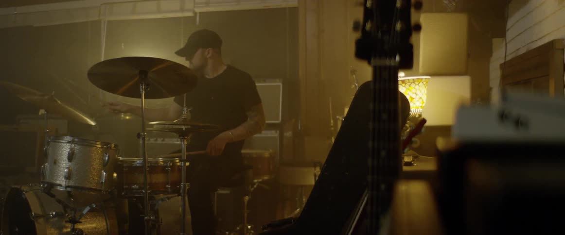 A man played drums in a small room in warm lamp light