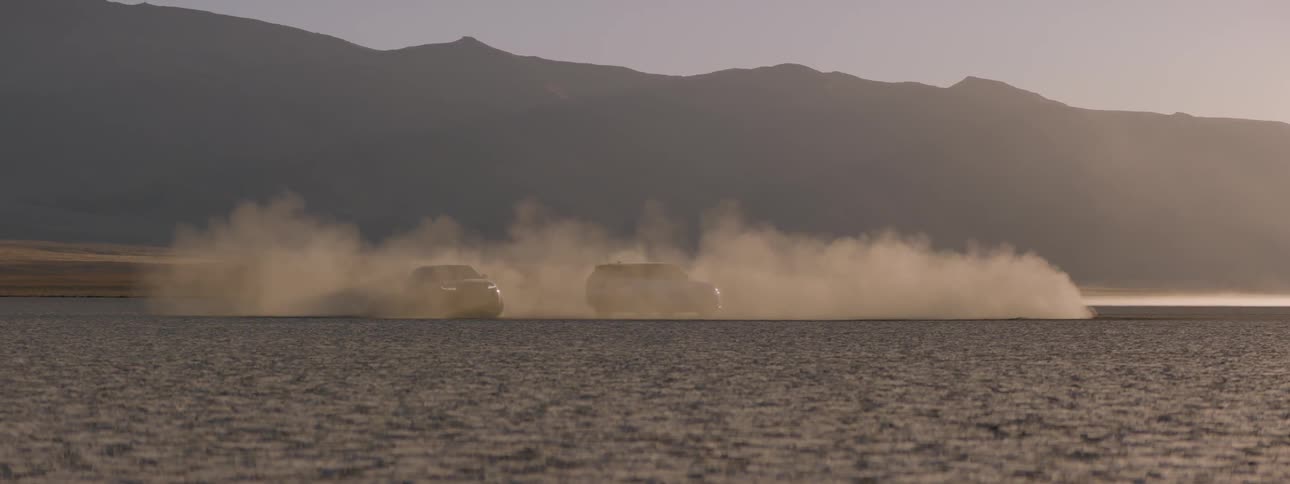 One range rover sport sits still while another drives in circles in the dust cloud
