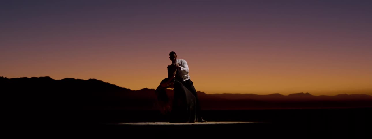 A man and a woman dancing on a stage outdoors at dusk
