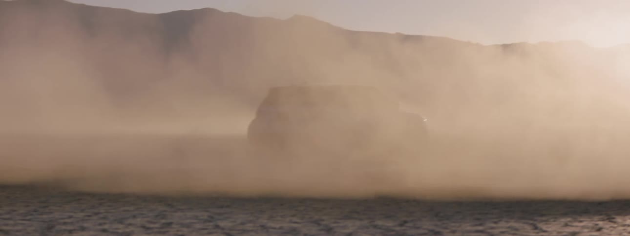 A rolling cloud of dust obscures two suvs on the salt flats