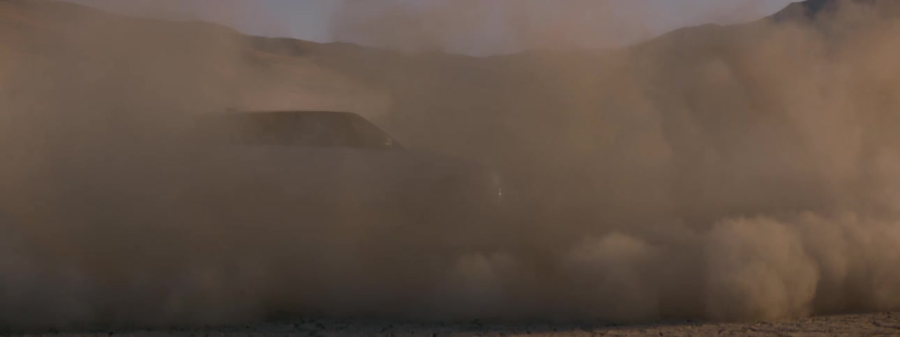 A vehicle driving circles around another vehicle while raising dust in the desert