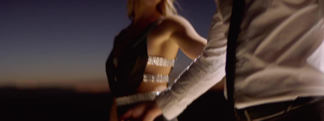 A woman walks around in a man in a circle and runs her hand down his arm to take his hand