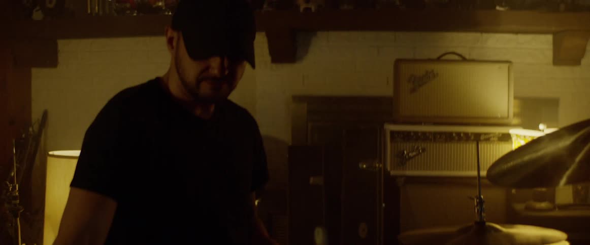 A drummer walks over to a drum kit in a softly lit studio
