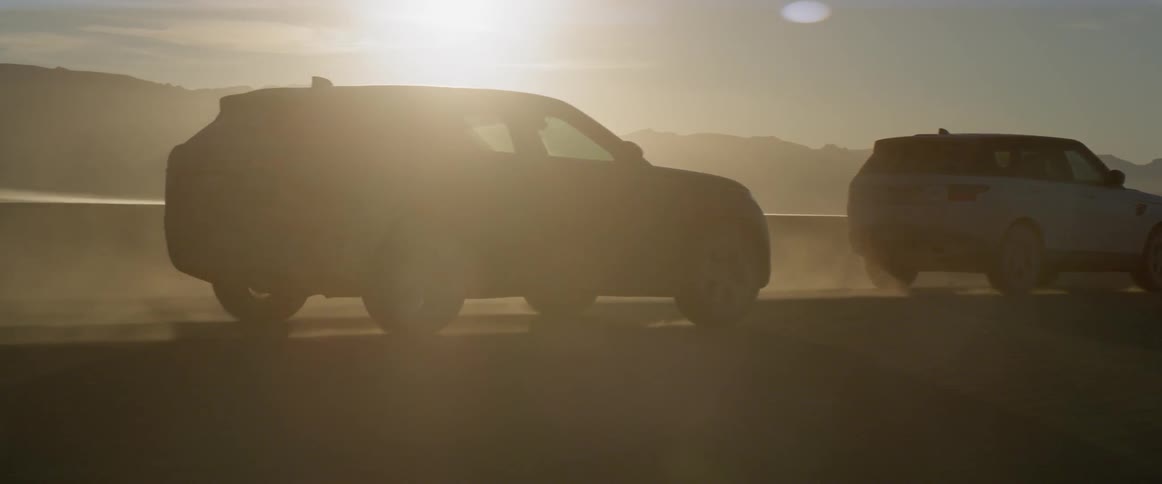 Two range rover sports drive across the desert at sunset