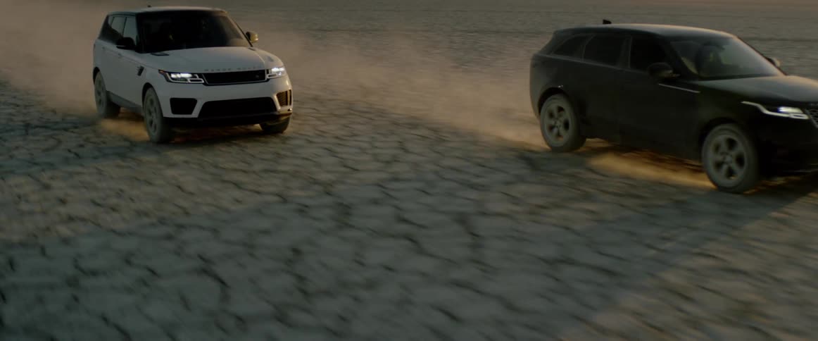 Two sports utility vehicles drive on the salt flats in the evening
