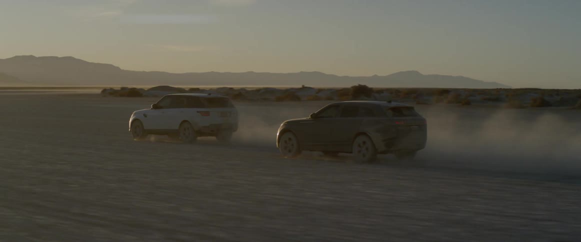 Two vehicles travel through the desert stirring up dust
