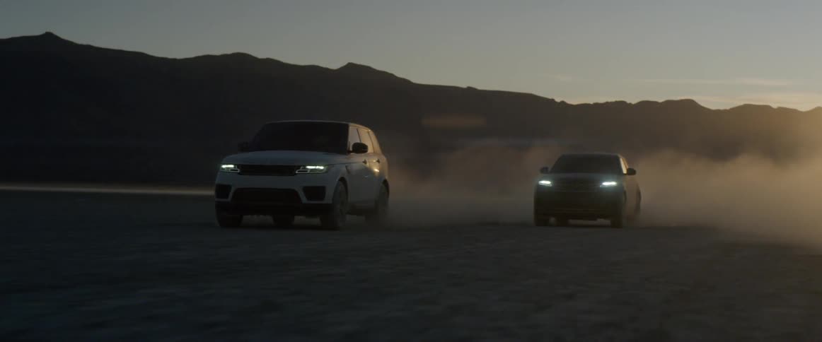 Two suvs on the salt flats kicking up dust at sunset