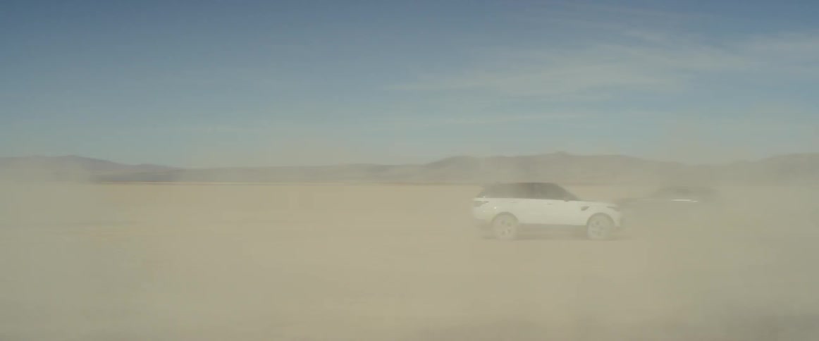 Two range rover sports drive in circles on the salt flats creating a  huge dust cloud