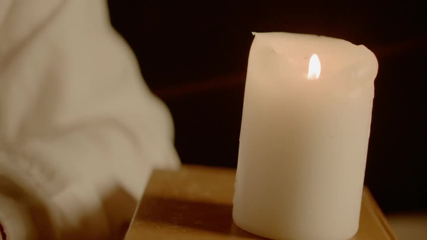A person sits next to a burning candle