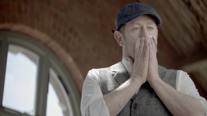 A white man takes a handkerchief out of his vest pocket and blows his nose into it
