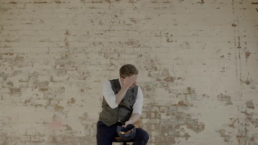 A sad man sitting in front of a brick wall