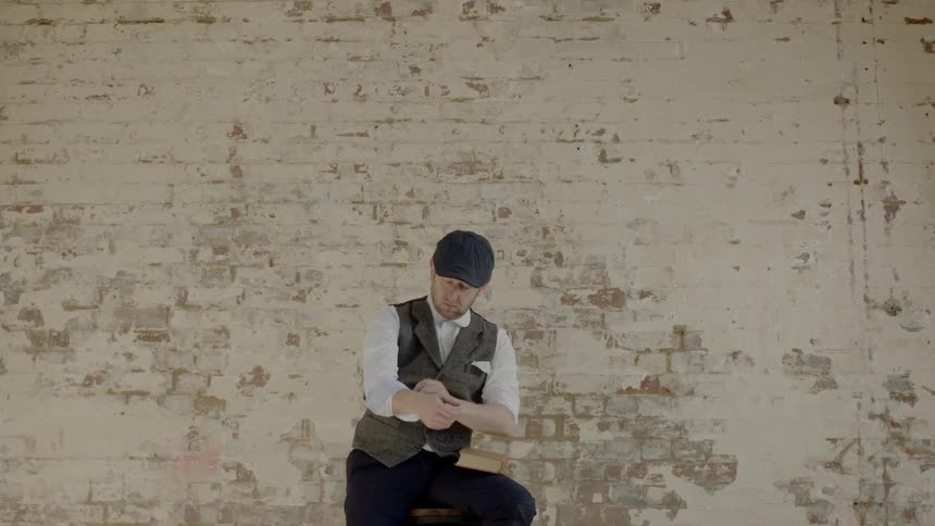 Man in a cap sitting on a stool near a wall rolling up his sleeves