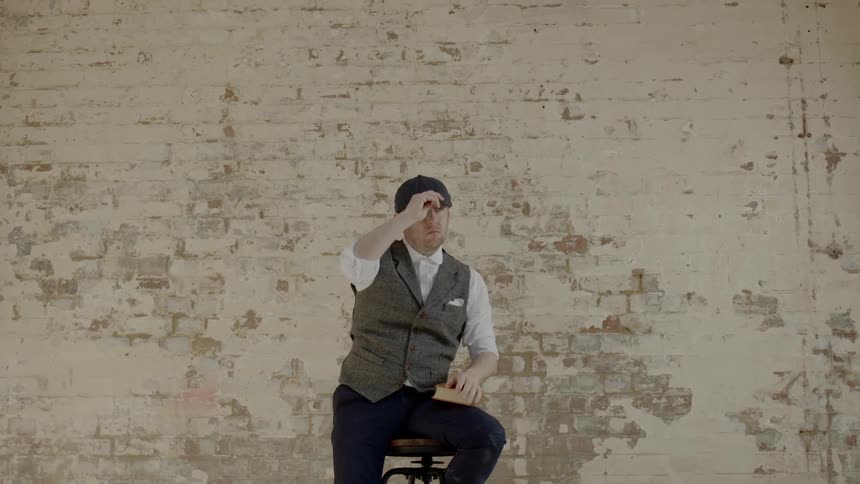 A man sitting on a stool puts a cap on his head