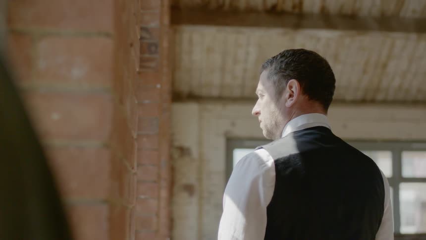 Man wearing a shirt and black waistcoat looks out the window in a building
