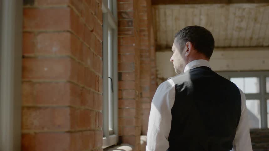A man standing next to and looking out the window of a brick building
