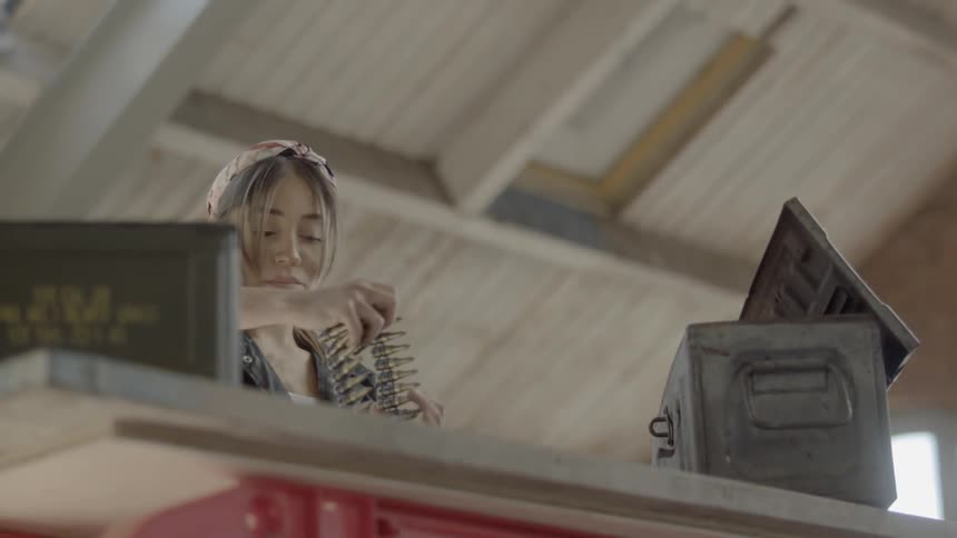 A woman pulls an ammunition belt out of a metal box
