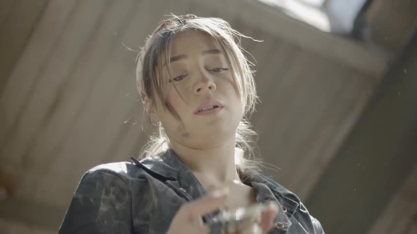 A woman covered in grime throws a belt of ammunition over her shoulder
