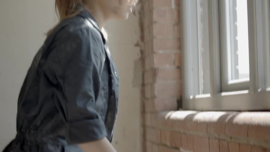 A woman puts down the handle of a tackle box then stands up and looks through a window