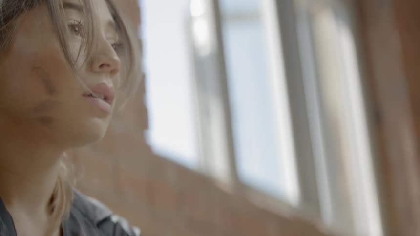 A sad looking young woman sitting on the floor raises her head and looks into the distance