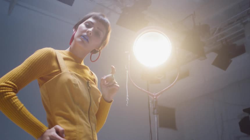 A woman stands in a studio under a large studio light