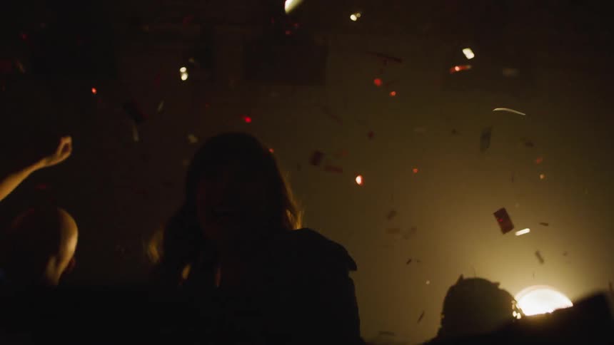 A group of women in a studio filled with bright lights jump up and down as they celebrate and confetti falls all around them
