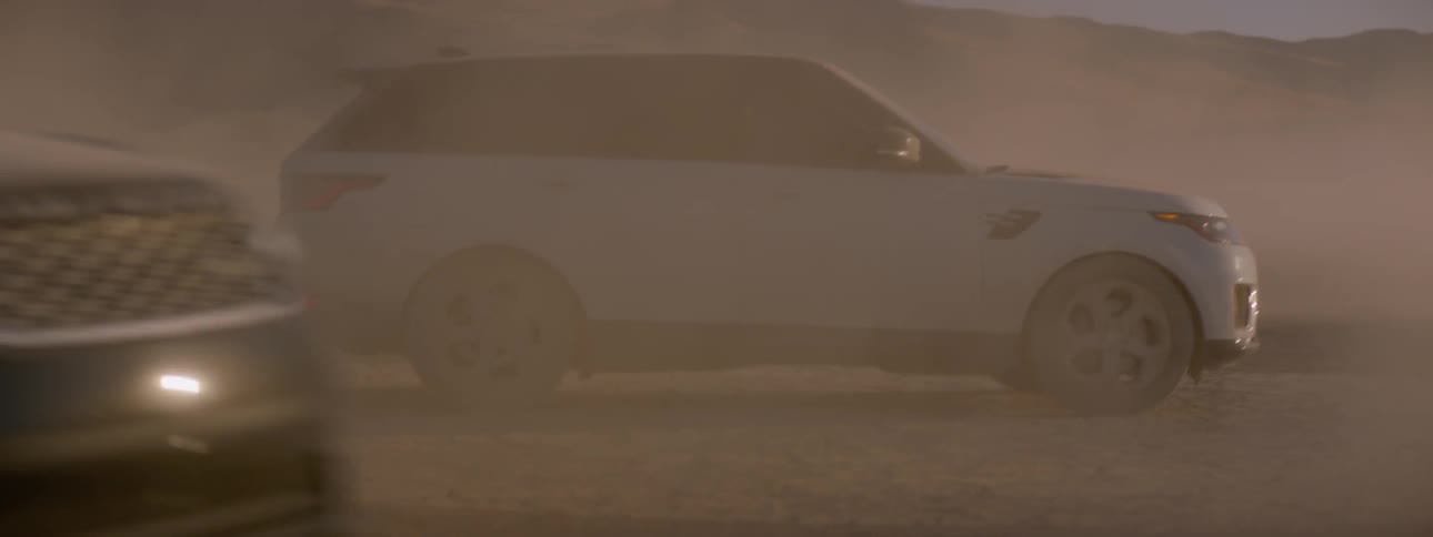 A white suv is pakred on the salt flats as a black range rover sport drives around it to park
