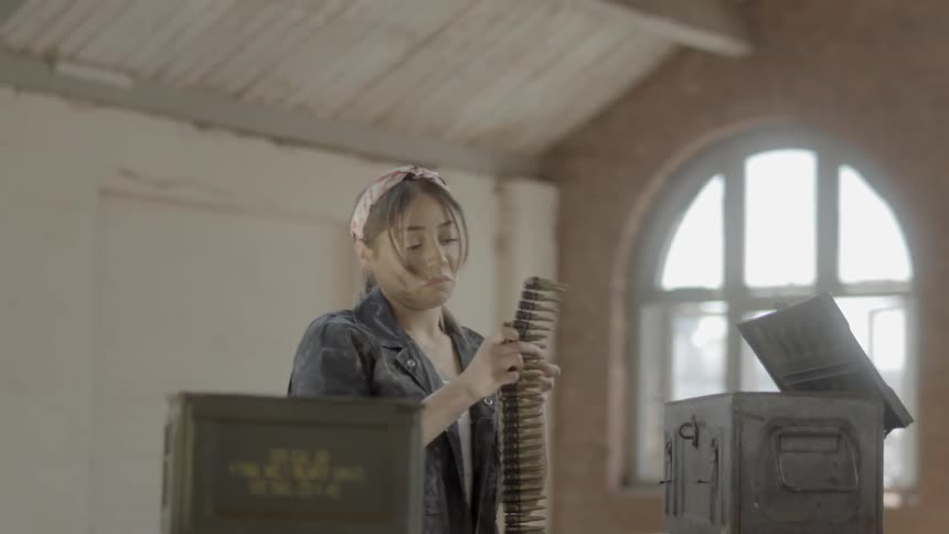 A woman takes an ammo belt out of an ammunition crate and lays it flat on a table